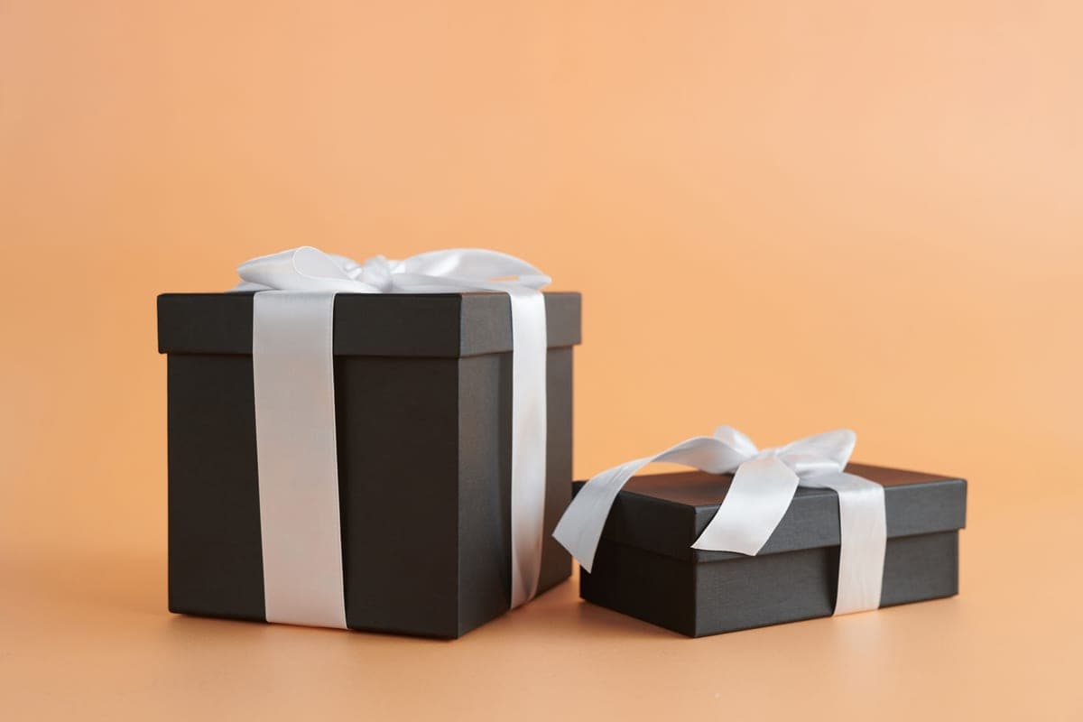 Two black gift boxes with white ribbons on a beige background