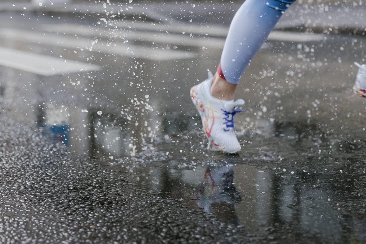 A runner's sneakers splashing through puddles on a wet street