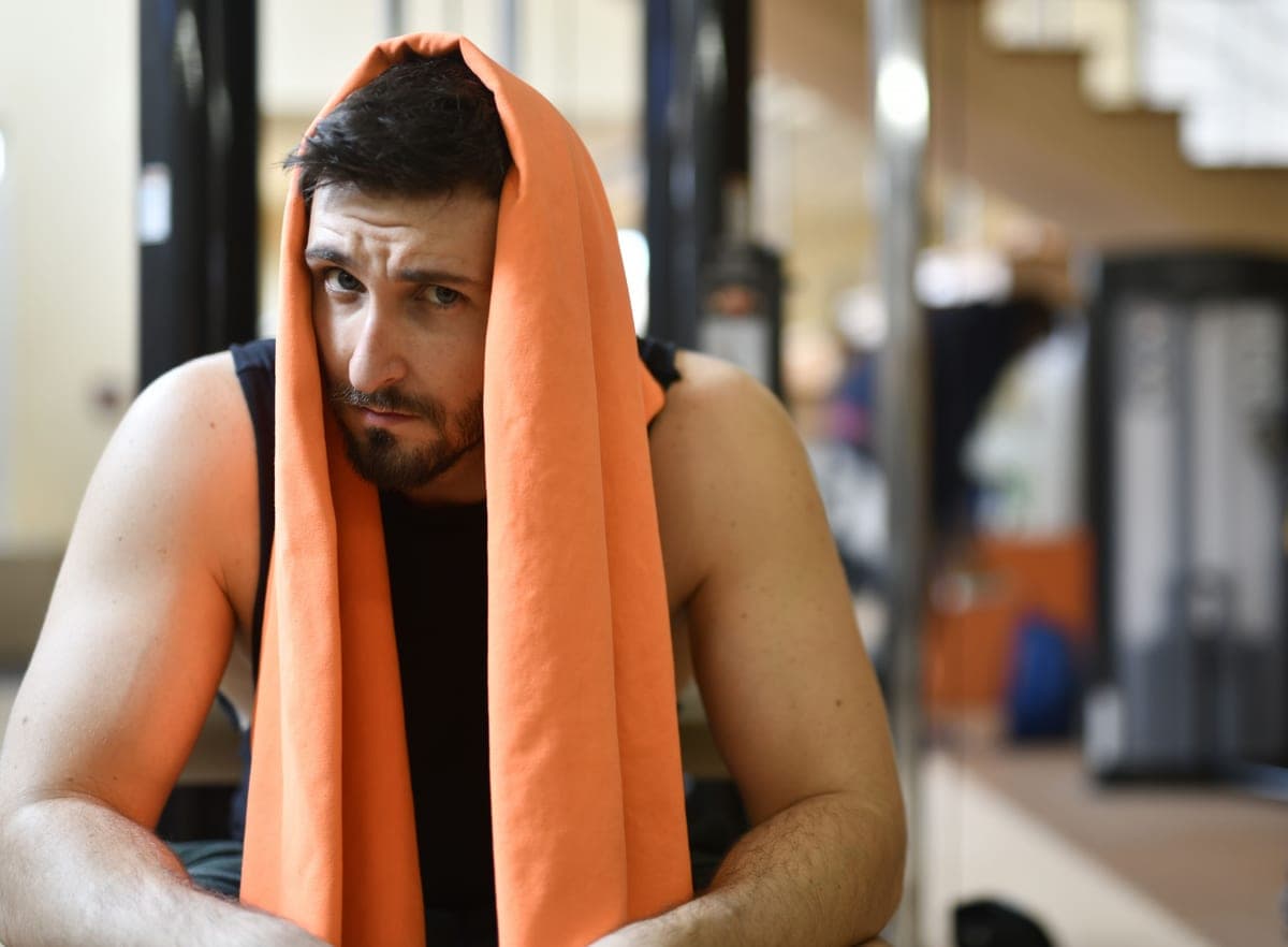 A tired man resting with a towel over his head after a gym workout